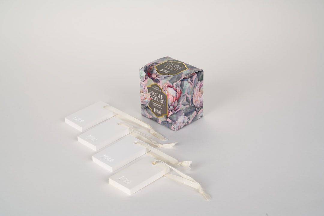 Four white rectangular scented chalk tags with ribbons beside a floral patterned box (photographie d’illustration)