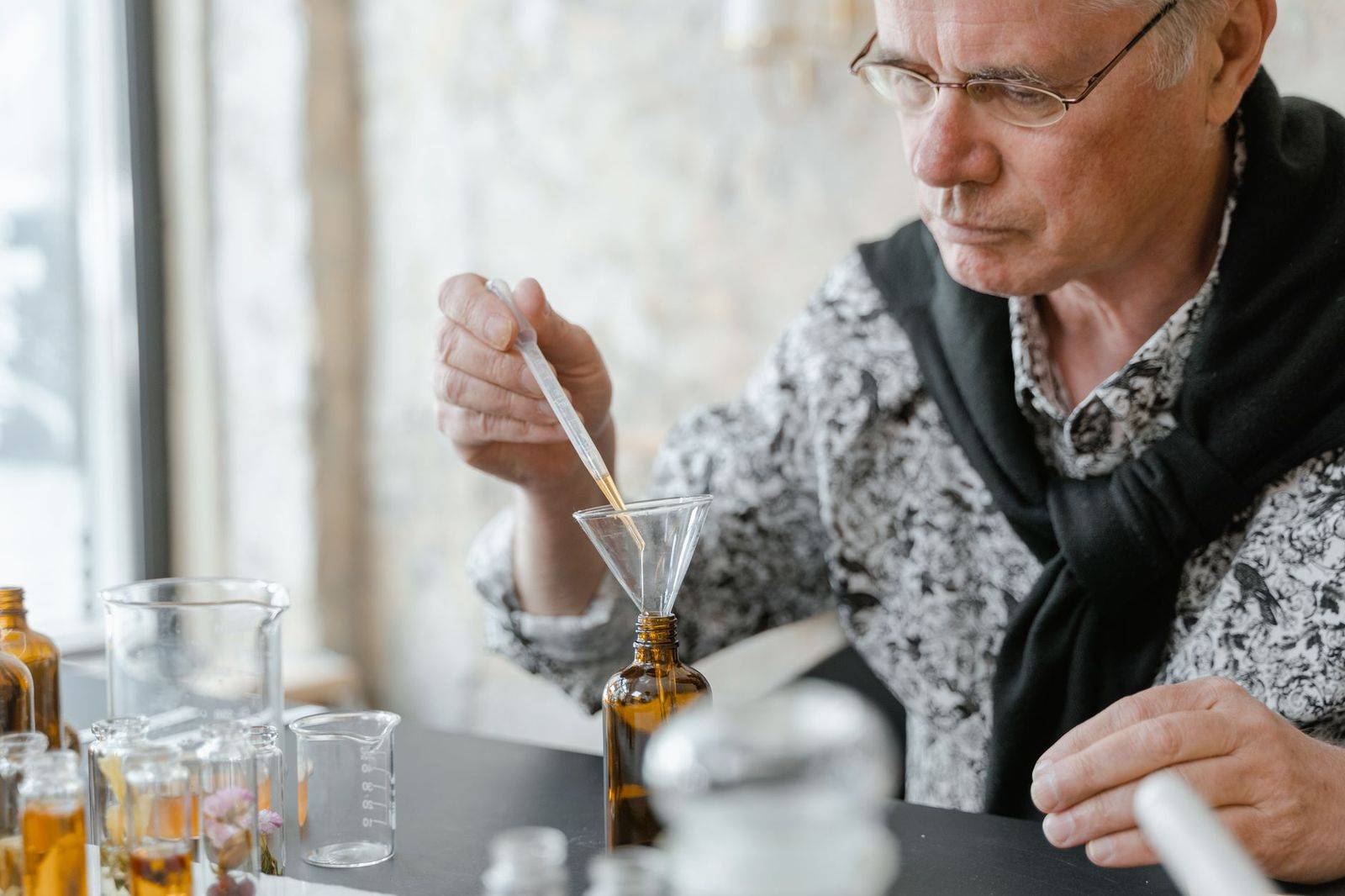 Senior adult blending essential oils using a dropper and brown glass bottles in a cozy indoor setting. (photographie d’illustration)