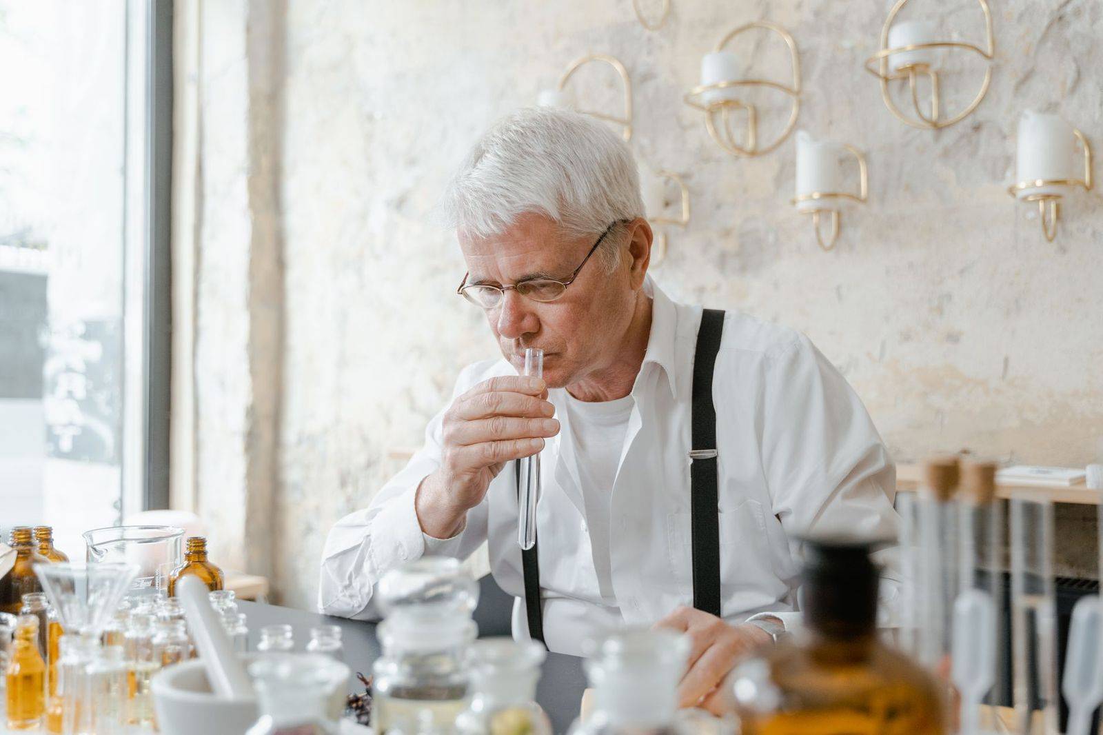 Senior man carefully smelling a test tube amidst laboratory glassware indicating a chemical experiment. (photographie d’illustration)