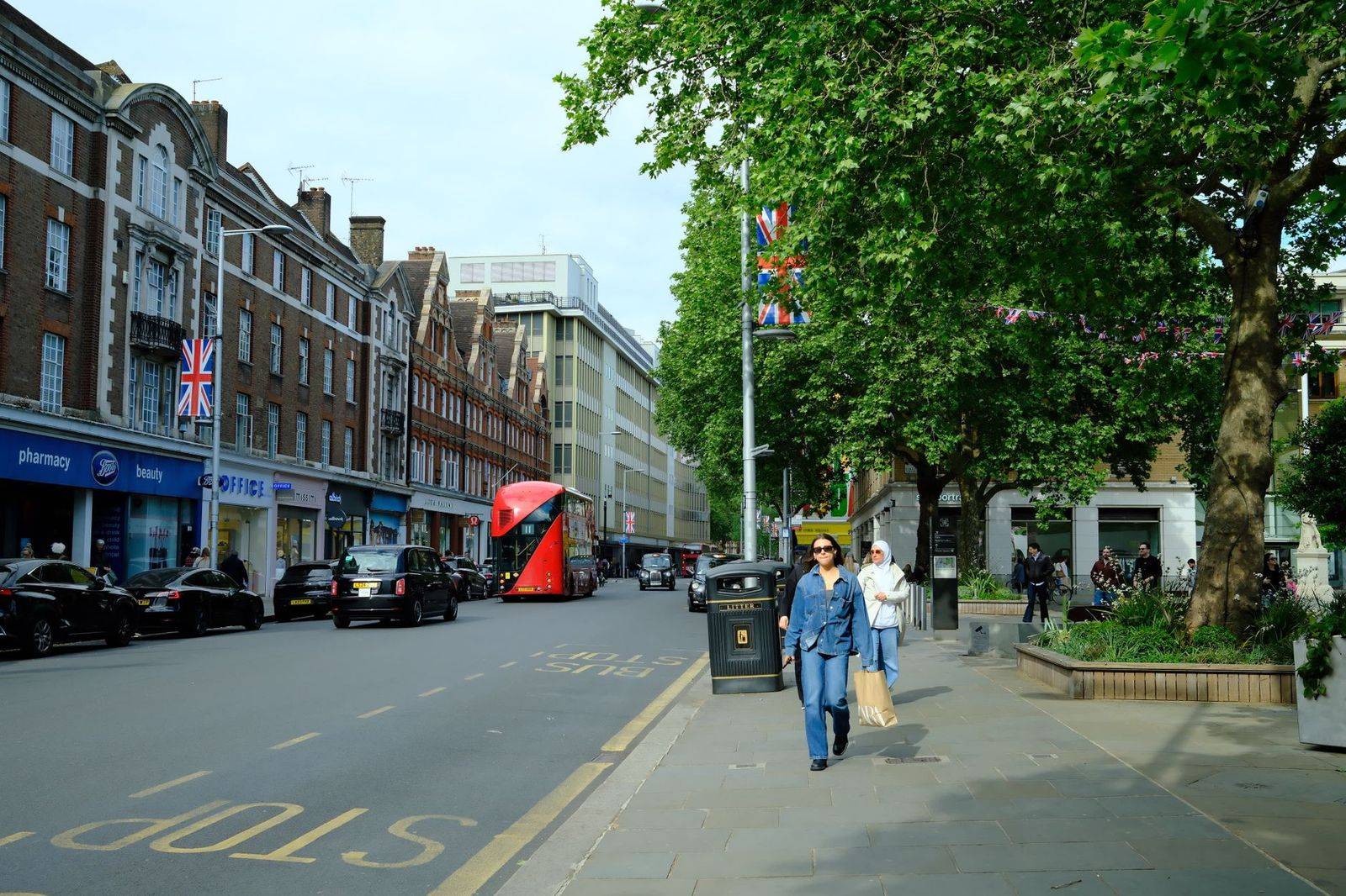 Lively street scene in London with a red bus, shops, and pedestrians. (photographie d’illustration)