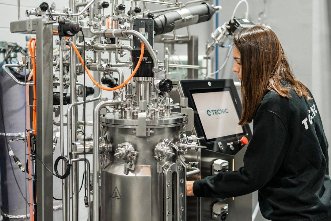 Operator handling a stainless steel bioreactor with integrated touch screen in a technical process control environment. (photographie d’illustration)