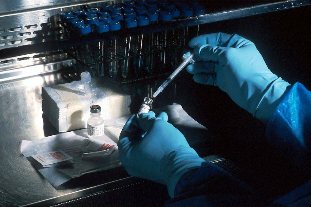 Vaccine. Hands of a scientist, under a sterile hood, preparing the carcinoembryonic antigen (CEA) vaccinia used to try to prevent cancer. The scientist is diluting the concentrated vaccinnia virus into a dose level appropriate for administration to a patient. This vaccinnia marks any cancer cells expressing the CEA. (photographie d’illustration)