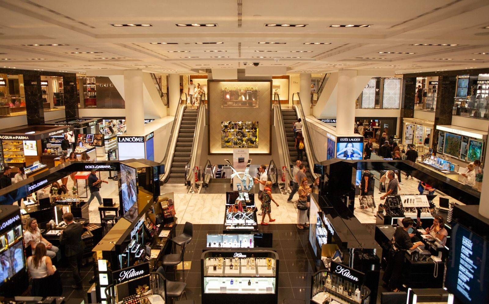 A bustling scene inside a modern shopping mall with escalators and various retail stalls. (photographie d’illustration)